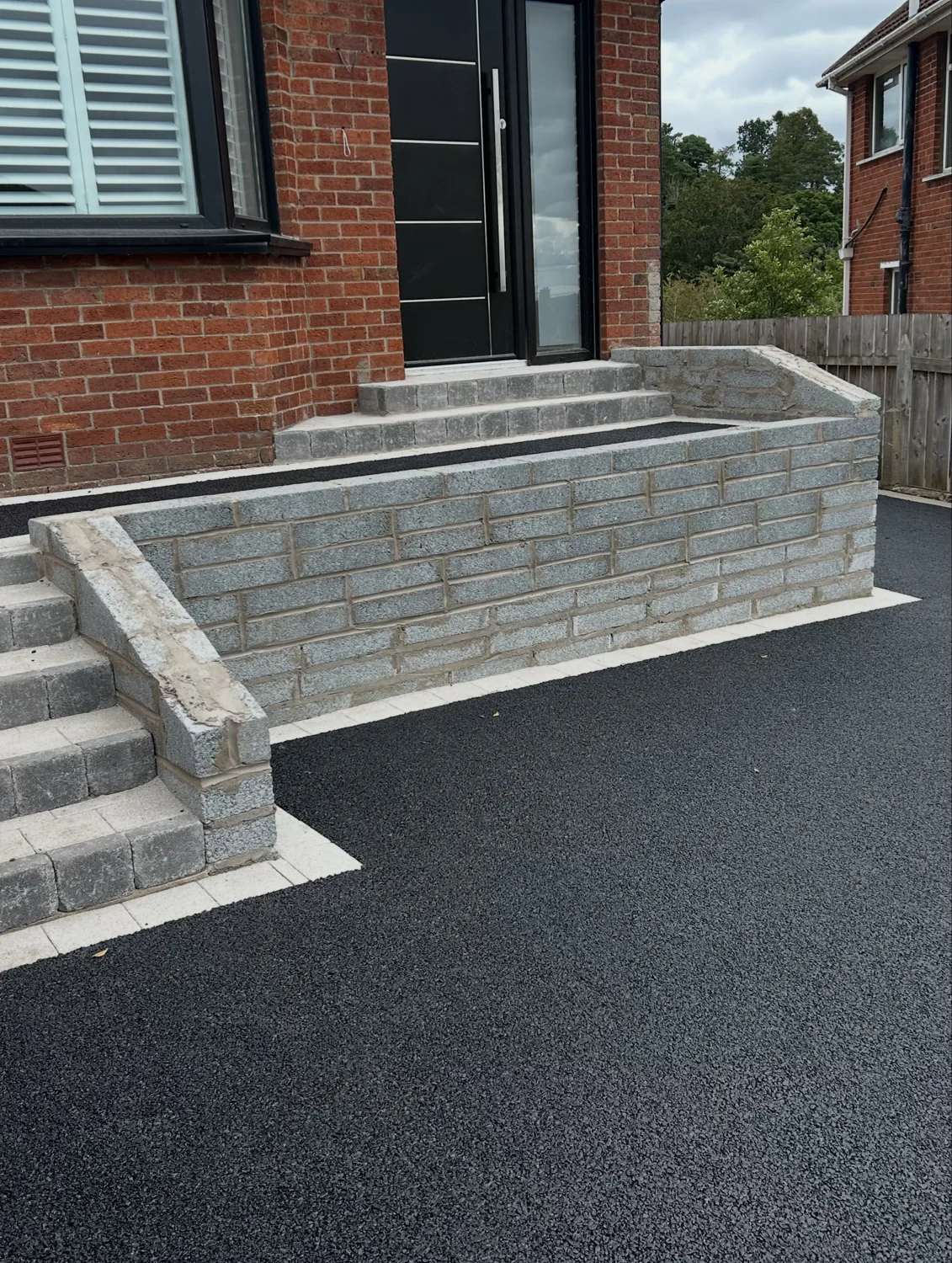 A driveway with grey retaining walls, charcoal steps and a brick border