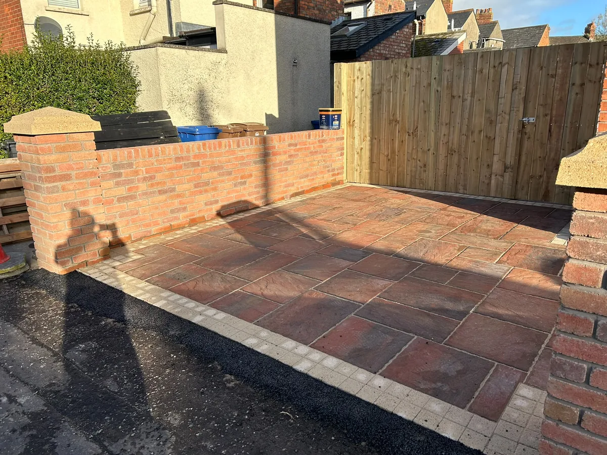 Warm-toned front paving with a pale contrasting border beside brick walls and a timber gate